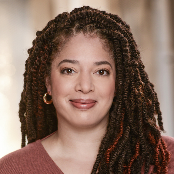 A smiling headshot of Rebecca Singh. She is a mixed race woman with long brown hair styled in twists